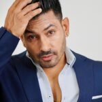 Elegant man in blue suit adjusting hair, exuding confidence and style.